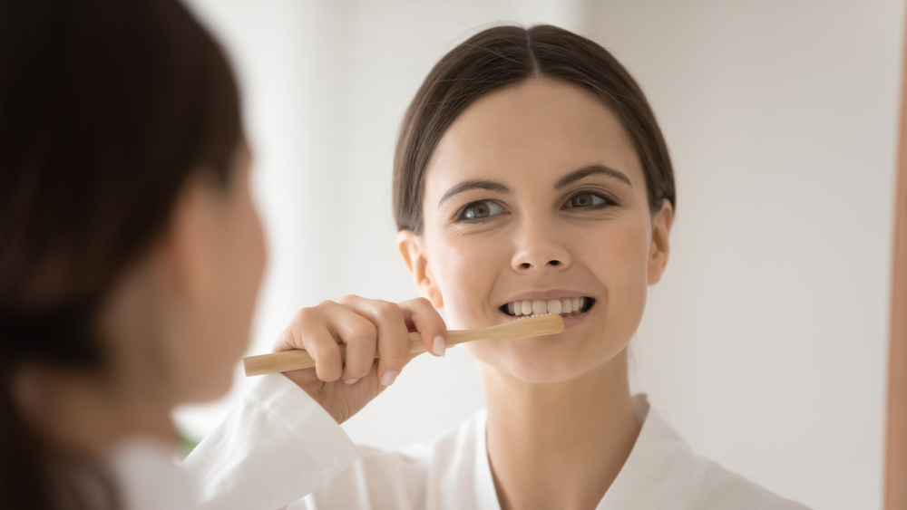 Woman brushing her teeth with a bamboo toothbrush to maintain her smile after cosmetic dentistry