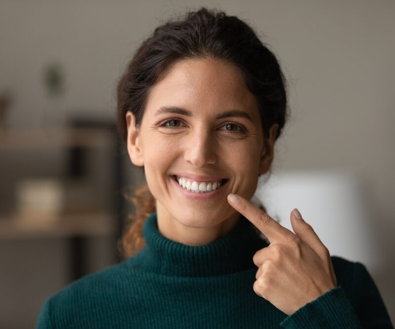 Woman pointing to her bright, white smile while comparing the differences between dental implants and veneers