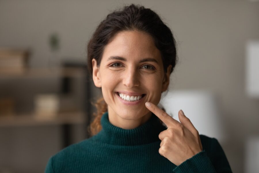 Woman pointing to her bright, white smile while comparing the differences between dental implants and veneers