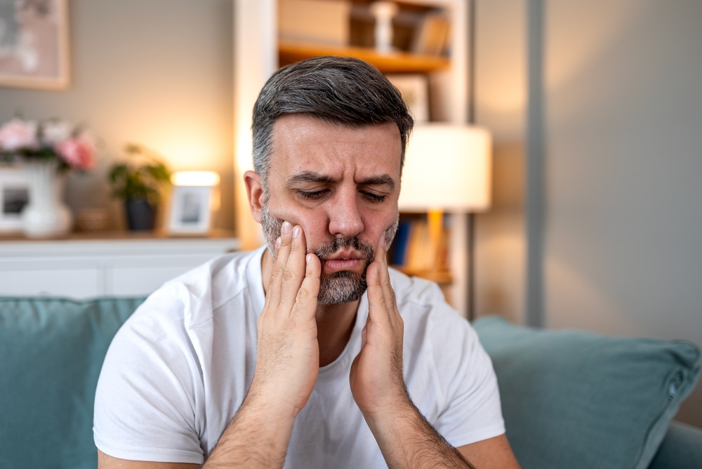 Man wincing in pain and holding both hands to his jaw, showing signs of a dental emergency that need immediate care