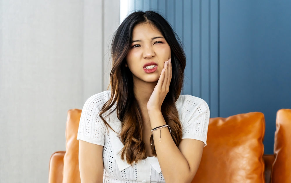Young woman wincing in pain and holding her cheek due to a toothache, in need of an emergency dentist