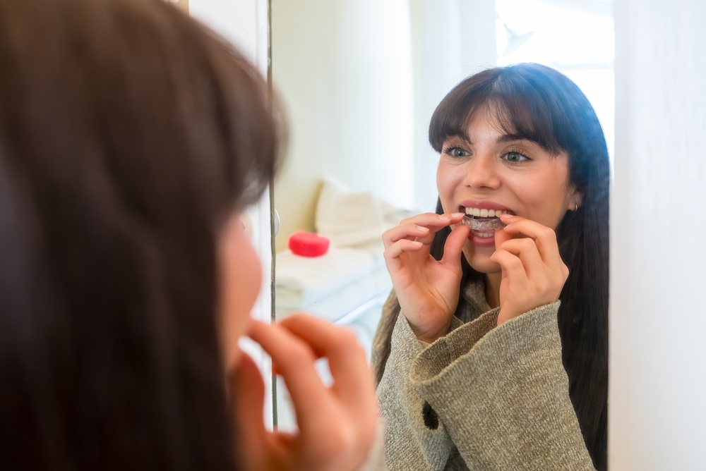 Woman inserting a clear aligner at her bathroom mirror