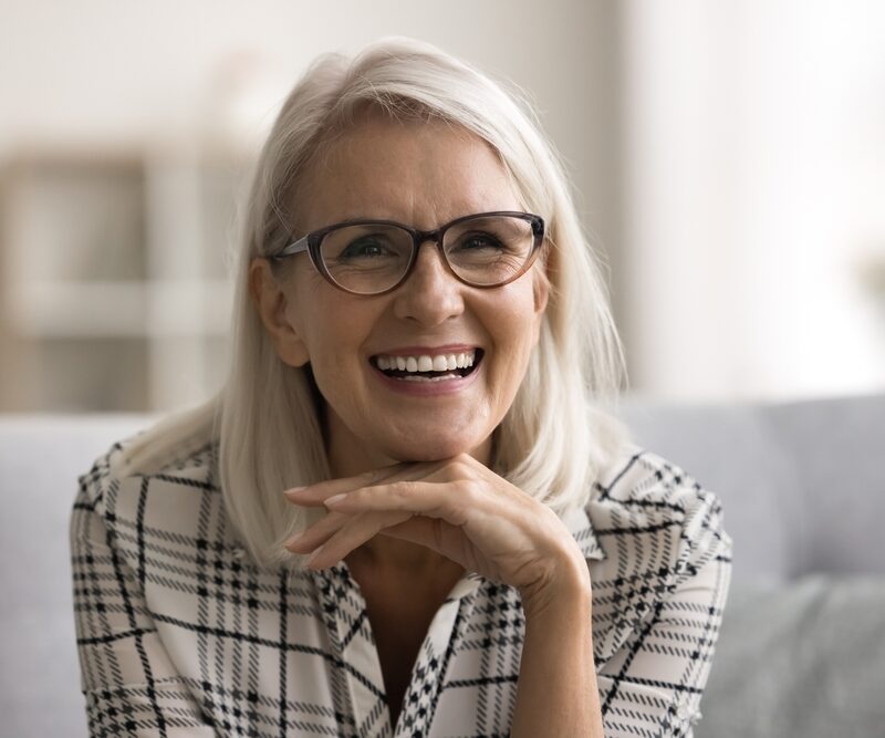 Smiling mature woman with glasses resting her chin on her hand, reflecting the confident results of choosing the right dental solution