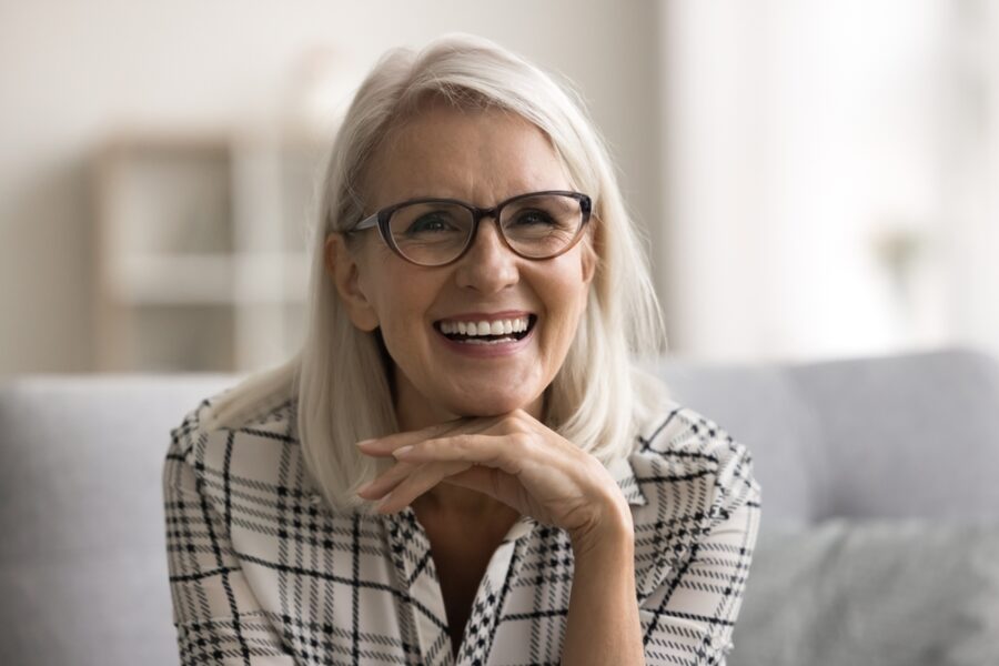 Smiling mature woman with glasses resting her chin on her hand, reflecting the confident results of choosing the right dental solution