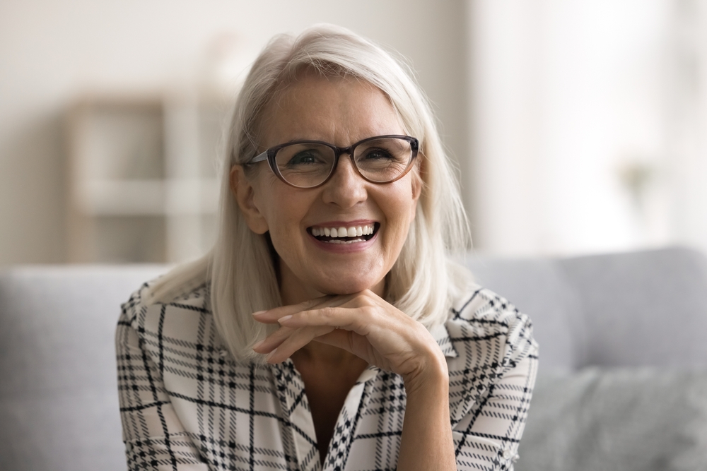 Smiling mature woman with glasses resting her chin on her hand, reflecting the confident results of choosing the right dental solution