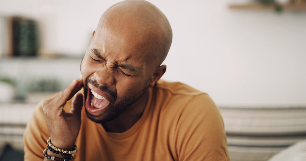 Man wincing in pain and holding his jaw due to a toothache, in need of emergency dental care