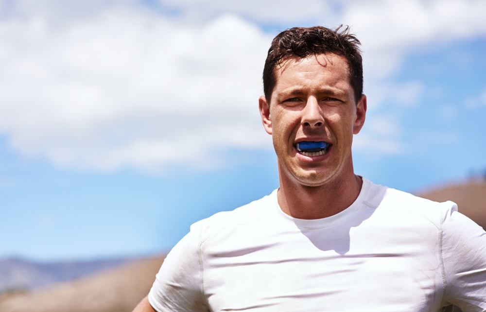 Man wearing a custom blue mouthguard outdoors during athletic activity, protecting his smile with a PlaySafe sports mouthguard from Bagoff Dental Arts